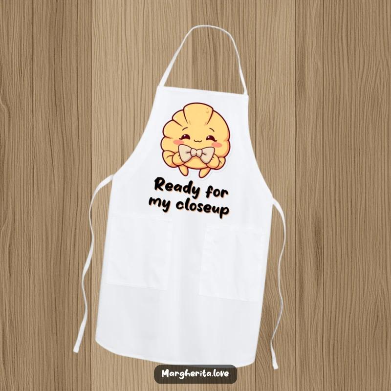 Funny apron featuring a curious croissant character in a dramatic, theatrical bow, perfect for kitchen use and as a humorous gift.